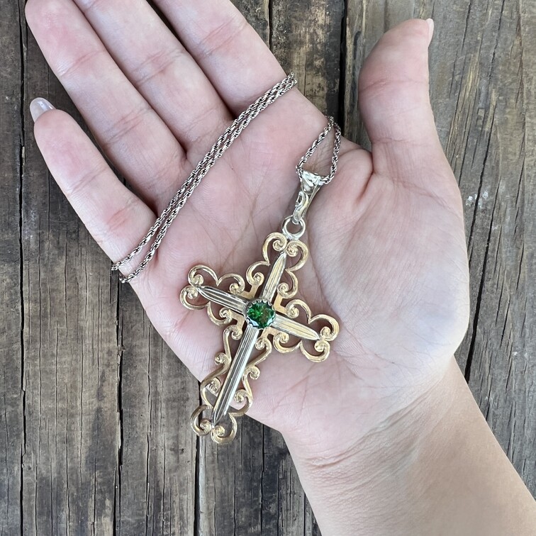 A golden cross pendant necklace with a simulated emerald and golden bronze